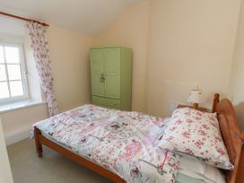 A small bedroom with a single bed a wooden headboard a green wardrobe floral bedding and a window with floral curtains at Northgate Cottage in Ysceifiog near Caerwys
