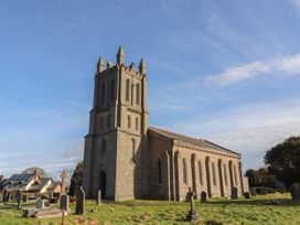 An old stone church with a tall bell tower and surrounding gravestones in a grassy area at Northgate Cottage in Ysceifiog near Caerwys