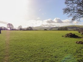 A green field with trees and hills in the background under a partly cloudy sky at Northgate Cottage in Ysceifiog near Caerwys