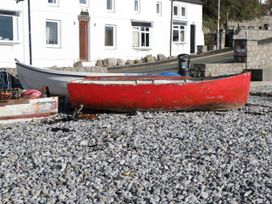 A red boat on pebbles near a building at Hunters Cottage in Benllech
