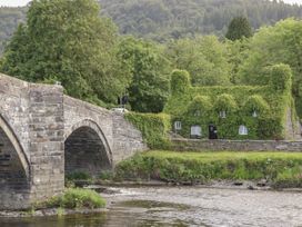A stone bridge over a river next to a house covered in green ivy with trees and hills in the background at Ysgubor Newydd in Henryd near Conwy