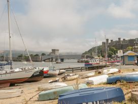 A harbor with boats on the shore and water near a bridge and castle at Ysgubor Newydd in Henryd near Conwy