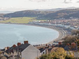 A coastal town with houses, a curved beach, and green hills in the background at Ysgubor Newydd in Henryd near Conwy