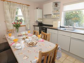 A kitchen with a dining table set with teacups and desserts and a window with curtains at Ysgubor Newydd in Henryd near Conwy