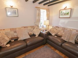 A corner seating area with brown leather sofas and patterned cushions near a window with curtains at Ysgubor Newydd in Henryd near Conwy