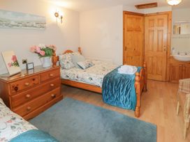 A bedroom with two single beds a wooden dresser with flowers a mirror and clock a blue rug and a corner sink at Ysgubor Newydd in Henryd near Conwy