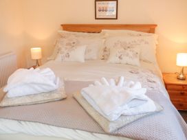 A bedroom with a double bed with floral bedding two bedside tables with lamps and folded towels on the bed at Ysgubor Newydd in Henryd near Conwy