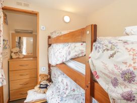 A bedroom with wooden bunk beds floral bedding a chest of drawers with a mirror and teddy bears at Ysgubor Newydd in Henryd near Conwy