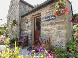A stone cottage entrance with two wooden chairs and hanging flower baskets at Ysgubor Newydd in Henryd near Conwy