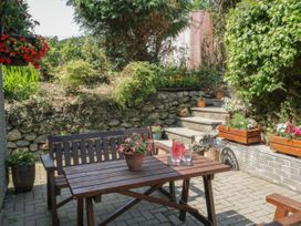 An outdoor patio area with wooden table and bench surrounded by potted plants and stone steps at Ysgubor Newydd in Henryd near Conwy