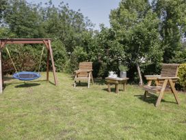 A garden with two wooden chairs a small wooden table with a teapot and flowers and a round blue swing at Ysgubor Newydd in Henryd near Conwy