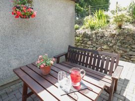 An outdoor seating area with a wooden bench and table with a pitcher of red drink and flowers at Ysgubor Newydd in Henryd near Conwy