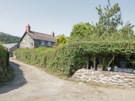 A stone house with chimneys behind a hedge and a gravel driveway at Ysgubor Newydd in Henryd near Conwy