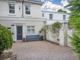 Front yard with a bench and potted plants outside a cream house with a blue door at Barwood View in Torquay