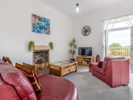 A living room with red leather sofas a wooden coffee table a tv stand with a television and an open door leading to a balcony at Barwood View in Torquay