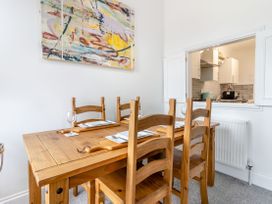 A dining room with a wooden table set for four and an open window to a kitchen at Barwood View in Torquay