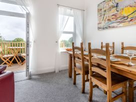 A dining area with a wooden table set for four and wooden chairs next to a window and open door leading to a balcony with a table and chairs at Barwood View in Torquay