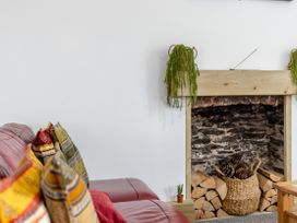 A fireplace with stacked firewood and a basket of pinecones next to a red sofa with colorful cushions at Barwood View in Torquay