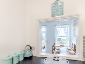 A kitchen counter with teal canisters and kettle with a window opening to a dining room with a table set with glasses and plates at Barwood View in Torquay