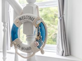 A decorative life buoy with welcome on board text hanging on a white stair post near a window with grey curtains at Barwood View in Torquay