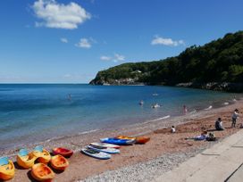 A beach with kayaks and paddleboards on the sand and people paddling in the sea at Barwood View in Torquay