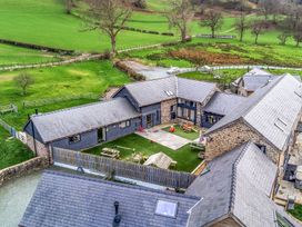 An outdoor view of a courtyard with multiple buildings and a grassy area at Bwthyn Y Bugail (Shepherd's Cottage) Pedairffordd near Llanrhaeadr-Ym-Mochnant
