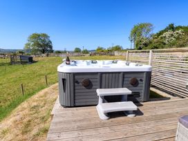 An outdoor hot tub on a wooden deck with grass and trees in the background at The Wren in Llysfaen