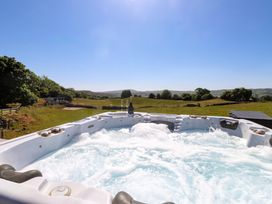 A bubbling outdoor hot tub with a bottle and two glasses overlooking a field and hills at The Wren in Llysfaen