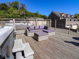An outdoor wooden deck with a sectional sofa with purple cushions and a hot tub at The Wren in Llysfaen