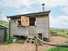 A wooden shepherd's hut with a half-open door and window on a grassy area with a picnic table in the background at Shepherd's Hut in Scarborough
