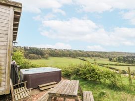 An outdoor area with a hot tub wooden bench wooden chair and a view of fields and trees at Shepherd's Hut in Scarborough