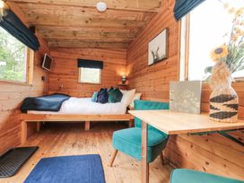 A wooden room with a bed with pillows and blanket two teal chairs a wooden table and a window with flowers at Shepherd's Hut in Scarborough