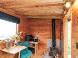 A wooden small room with a stove a teal chair a table with flowers and a kitchenette at Shepherd's Hut in Scarborough