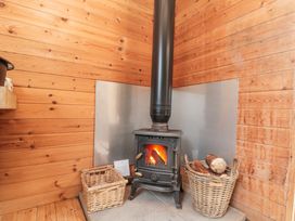 A wood stove with fire burning surrounded by wicker baskets of logs in a wooden room at Shepherd's Hut in Scarborough