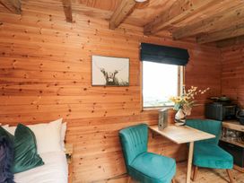 A small wooden room with a table between two green chairs and a bed on the left at Shepherd's Hut in Scarborough