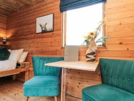 A wooden room with a small table between two teal chairs a bed with pillows and a framed picture on the wall at Shepherds Hut in Scarborough