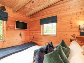 A bedroom with a bed green and purple pillows wooden walls windows with blue blinds and a wall-mounted television at Shepherd's Hut in Scarborough