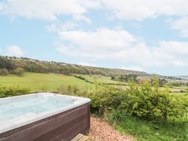 An outdoor hot tub next to a grassy area with bushes and a view of rolling hills and trees at Shepherd's Hut in Scarborough