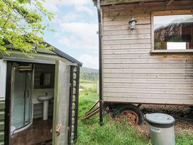 An outdoor scene with a wooden building on wheels and a small green structure with an open door showing a bathroom at Shepherd's Hut in Scarborough