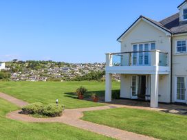 A two-story house with a balcony and patio on a lawn with a pathway and distant houses in South Milton near Thurlestone