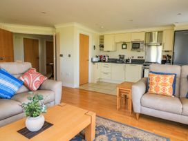 A living room area with beige sofas, colorful cushions, a wooden coffee table with a plant, and a kitchen with cream cabinets and appliances at 4 Thurlestone Beach House South Milton near Thurlestone