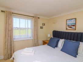 A bedroom with a bed with blue pillows beside a window with beige curtains at 4 Thurlestone Beach House in South Milton near Thurlestone