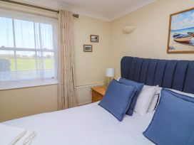 A bedroom with a bed with blue pillows beside a window with curtains and a nightstand with a lamp at 4 Thurlestone Beach House South Milton near Thurlestone