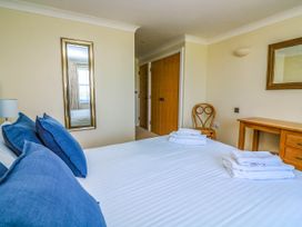 A bedroom with a bed, blue pillows, folded towels, wooden desk, chair, mirror and closed wooden closet doors at 4 Thurlestone Beach House in South Milton near Thurlestone