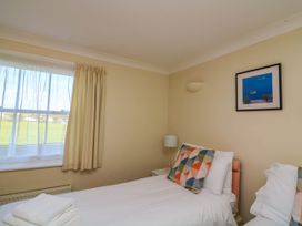 A bedroom with two single beds a window with curtains a bedside table with lamp and a framed picture on the wall at 4 Thurlestone Beach House South Milton near Thurlestone