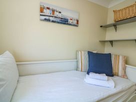 A bed with white sheets and pillows with a folded towel on it in a room with wall shelves and a painting on the wall at 4 Thurlestone Beach House South Milton near Thurlestone