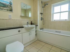 A bathroom with a bathtub shower combination a sink with storage cabinets a toilet and a window at 4 Thurlestone Beach House in South Milton near Thurlestone