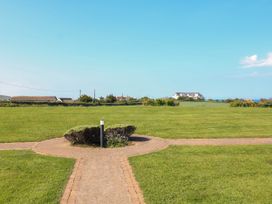 A grassy open area with a circular path and shrubs and houses in the distance at 4 Thurlestone Beach House in South Milton near Thurlestone