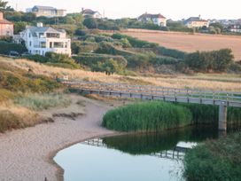 A wooden footbridge over a calm river with grass and houses on surrounding hills at 4 Thurlestone Beach House in South Milton near Thurlestone