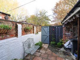 An outdoor patio area with a metal bench, brick walls with hanging planters, a blue wooden gate, and plants at 202 Salisbury Terrace in York